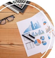 Top view of a desk with medical billing data analytics charts, graphs, and pie diagrams on paper, surrounded by a pair of glasses, pens, a calculator, and notebooks